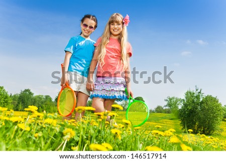 Two beautiful girls with tennis racquets standing in flower field