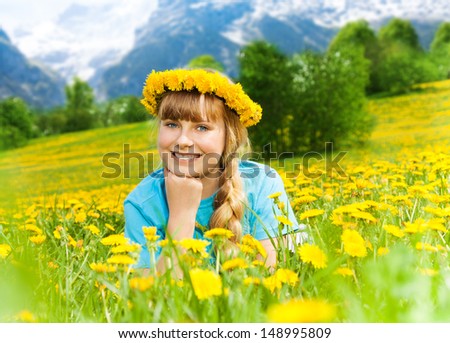 Happy beautiful smiling girl laying in mountain dandelion yellow flower field wearing wreath
