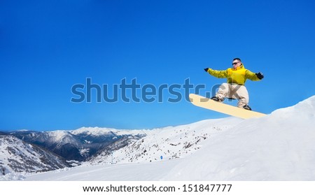 Cute handsome snowboarder man jumping from trampoline on snowboard in ski park in mountain resort