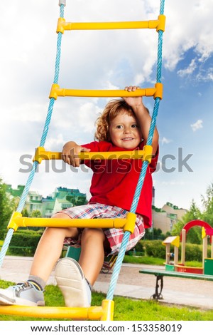 Happy little three years old child boy climbing on the rope ladder with sky on background