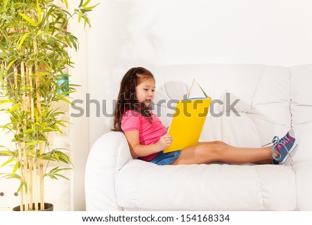 Beautiful Asian girl sitting on the couch and reading book looks very busy and occupied