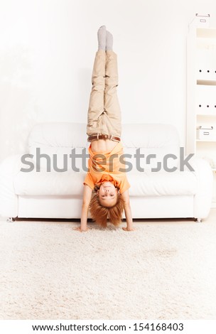 Cute little boy standing on the hands in living room by coach
