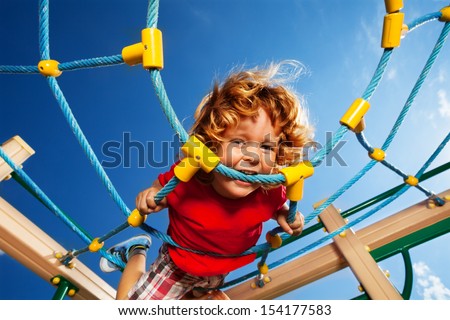 Strong expression of active of happy little three years old child boy biting the rope on the playground web
