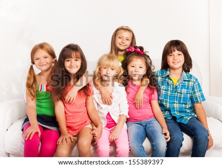 Large group of kids hugging, sitting together on the sofa at home and smiling
