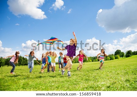Kids boys and girls with kite run in a large group together in the park on summer day with few clouds in blue sky