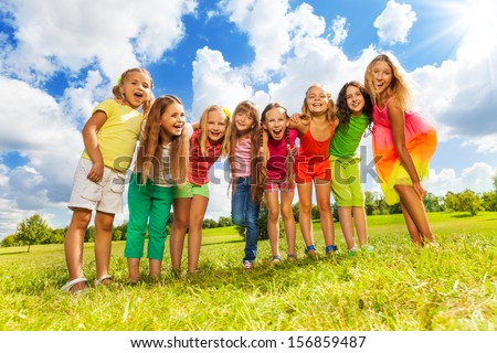 Large group of happy cute girls friends standing in a row in the park on the green grass on sunny summer day, hug and bend to camera