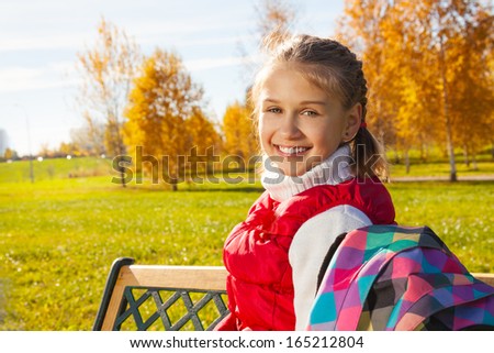 Close portrait of happy blond 11 years old girl with amazing smile turning back sitting on the bench in the autumn park on sunny day