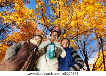 Group of four black kids, boys and girl, siblings, brothers and sister, smiling, laughing and looking down standing in autumn park