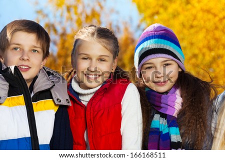 Close portrait of three happy kids, boy and two girls in autumn clothes on sunny day with happy smiling faces wearing warm clothes