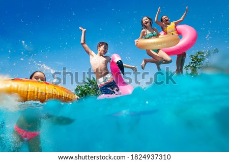 Half underwater split image of many little kids dive in the swimming pool throw inflatable toys lifting hands have fun