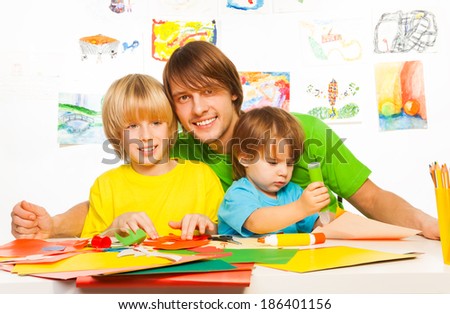 Happy dad with little kids cutting and gluing paper together with big smile on faces