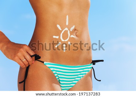 Close up of tanned cute belly with drawing of sun made of sunscreen cream