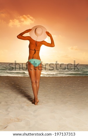 Beautiful fit woman wearing straw hat and beach at sunset