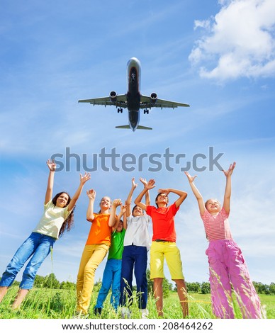 Excited children with hands up to plane in sky