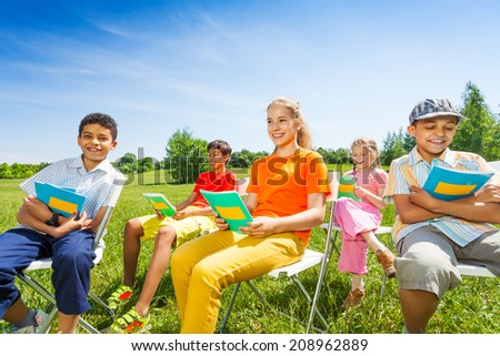 Happy kids hold exercise books and sit on chairs