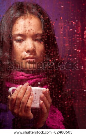 Thoughtful and a bit sad Asian woman in rainy weather with cup of hot tea behind the glass