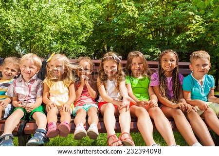 Front group portrait of group of kids sitting on the bench in the park, boys and girls 3-5 years old