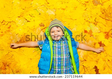Happy boy laying in orange autumn leaves