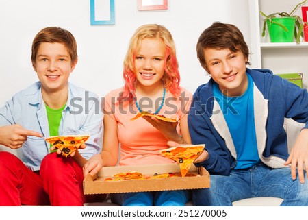 Three smiling friends hold pizza pieces and eat