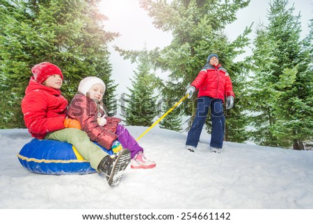 Happy kids sit on snow tube and other pulling them