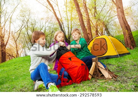 Three kids packing the things into red rucksack