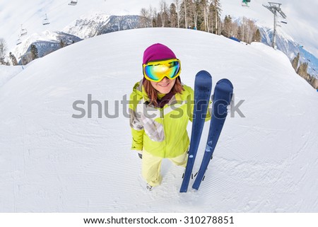 Smiling young woman in ski mask with ski from upper fisheye view and snow mountains on background in Sochi