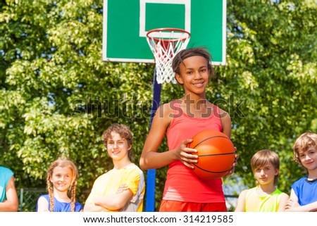 Smiling African girl with ball and friends behind