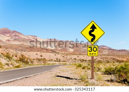 Road with arrow yellow sign in desert, California
