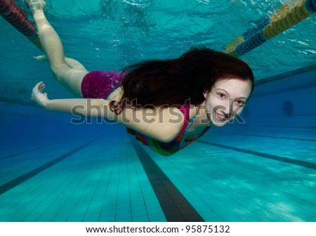 Young woman with long hair smiling swimming underwater in the pool