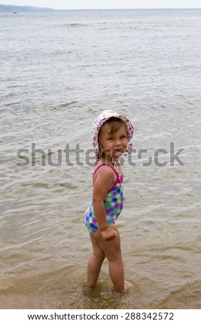 little white girl standing near the sea in a bathing suit and panama