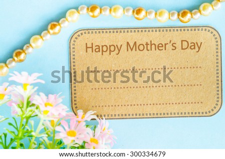 Happy mother\'s day on brown paper tag and pink flower on blue background for your text.