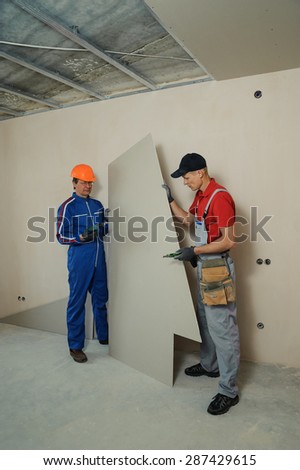 Drywall Installers. Men holding a gypsum board figured cut