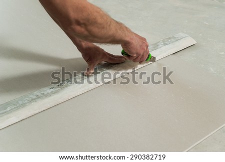 Man cuts off a piece of drywall with a knife and a ruler