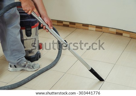 Worker cleans seams between tiles using a vacuum cleaner