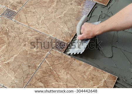 Laying Ceramic Tiles. Troweling adhesive onto a concrete floor in preparation for laying white floor tile.