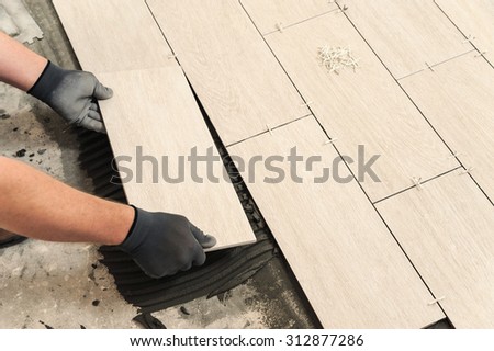 Laying Ceramic Tiles. Man placing ceramic floor tile in position over adhesive