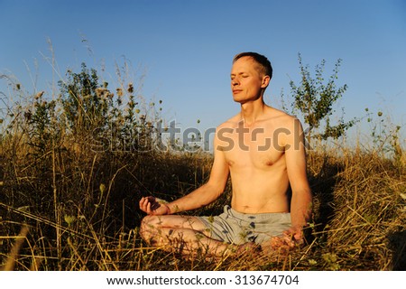 Man meditating. He sits in the grass with his legs folded under him