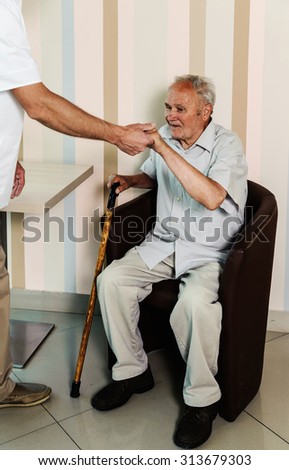 The doctor helping an old man get up from the chair