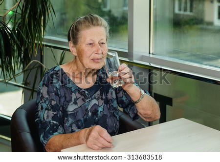 Elderly woman drinking water from a glass sitting at table