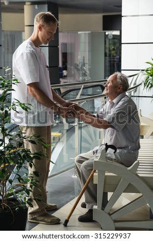 Health-care worker helps the elderly man get up from the bench