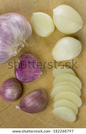 garlic bulb with garlic cloves and garlic slices on wooden cutting board.