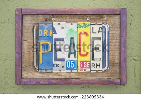 Peace sign made out of different state license plates in a wood frame hanging on concrete wall