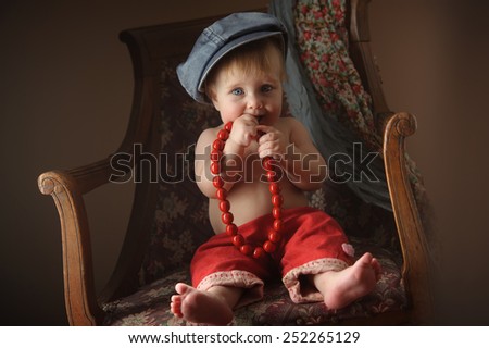 European little girl in a cap in the old chair. Up to 1 year.