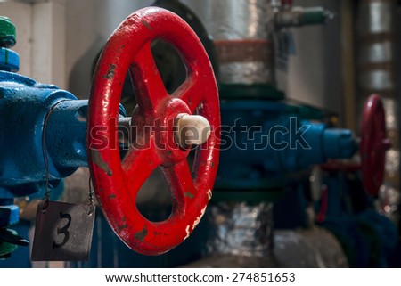 Red valve located on the flange of the blue pipe in the boiler room