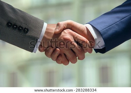 Handshake of two men in suits in front of a new home.
