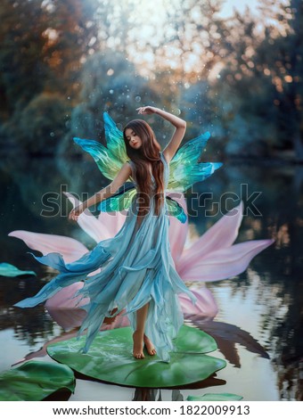 Beautiful young fantasy woman in image river fairy dances on water pink lily flower. long silk dress flies in wind motion butterfly wings magic shiny. Art Girl pixie. Background dark nature, blue lake