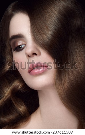 Beauty portrait of young girl with chestnut head, big green eyes, pouty lips with natural lipstick and curls falling on her eye looking to the right on black background