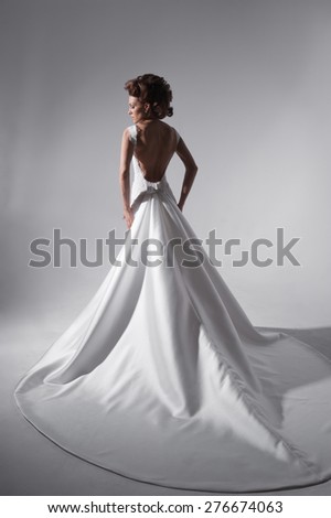 Young women in white floor-length dress, standing in the studio. Wedding dress. Plume.