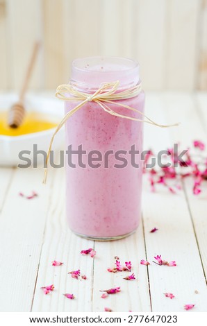 Pink Strawberry Smoothie in retro jar with purple flowers and honey on light rustic boards.