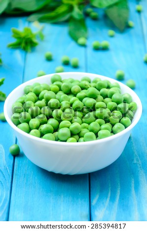RAW baby peas in small white bowl, over colorful turquoise blue painted wooden boards. Close-up